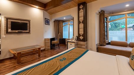 A spacious hotel room with a large bed, a TV, a desk, and a window with a view - DLS Meghavan Resort
